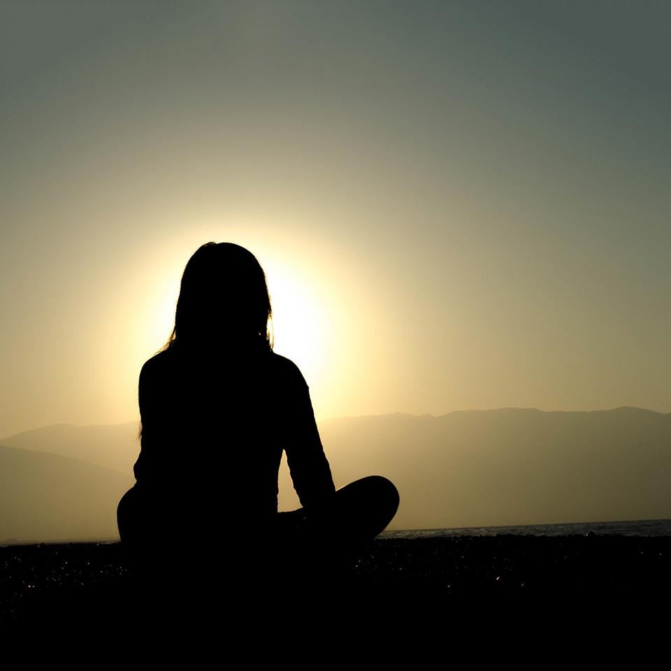 Silhouette einer Frau die im Sonnenuntergang zur Steigerung der Achtsamkeit meditiert.