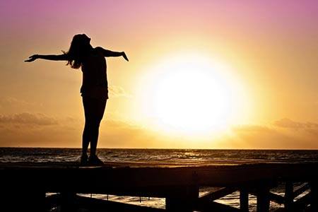 Frau steht auf einem Steg am Ufer, schaut in den Sonnenuntergang und kennt ihren Weg.