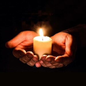 Eine weiße Kerze steht in den Handflächen beider Hände als Symbol für das Weihen von Kerzen zu Imbolc.