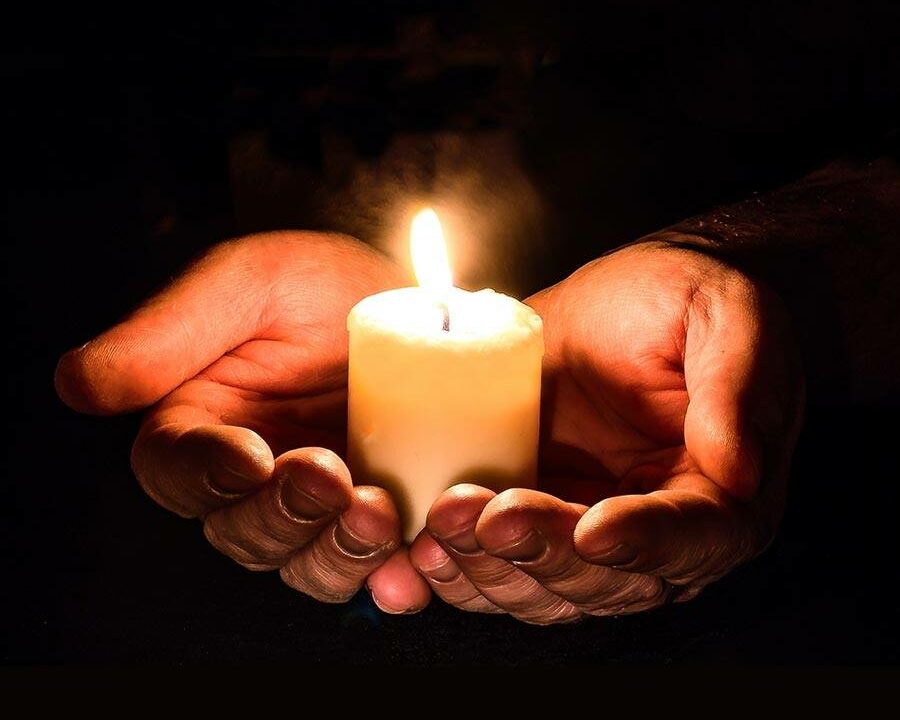 Eine weiße Kerze steht in den Handflächen beider Hände als Symbol für das Weihen von Kerzen zu Imbolc.