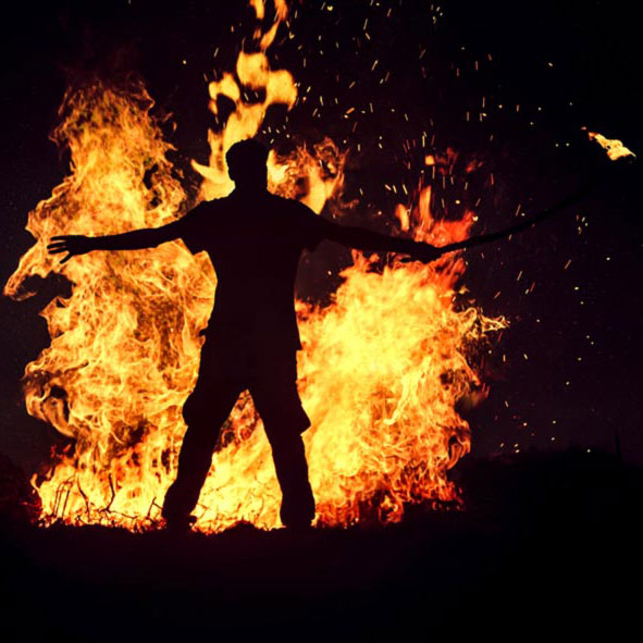 Ein Mann tanzt vor einem Freudenfeuer an Beltane