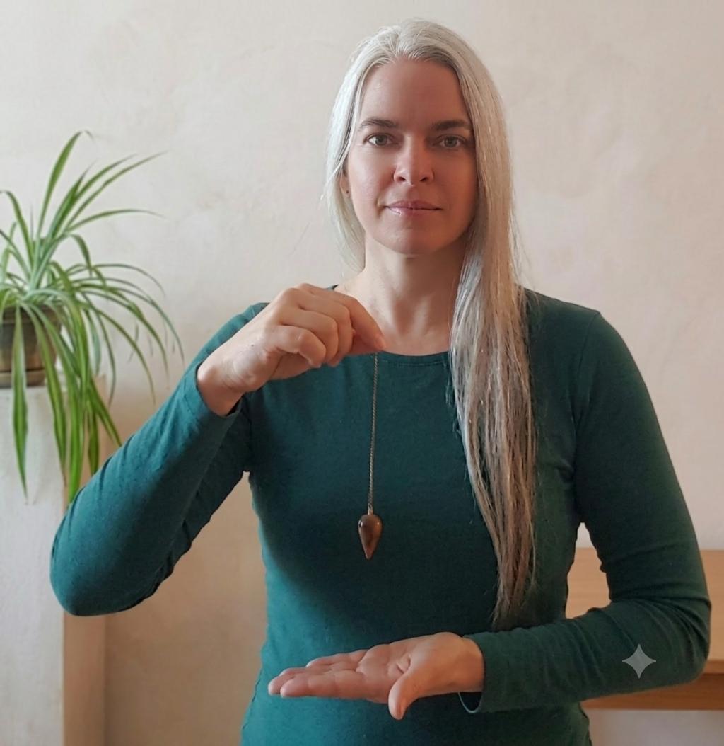 Daniela Dick lächelt in die Kamera und hält ein schwingendes Pendel - lernen mit dem Hexerey Workshop bei Dr. Daniela Dick. Online oder in Hamburg.